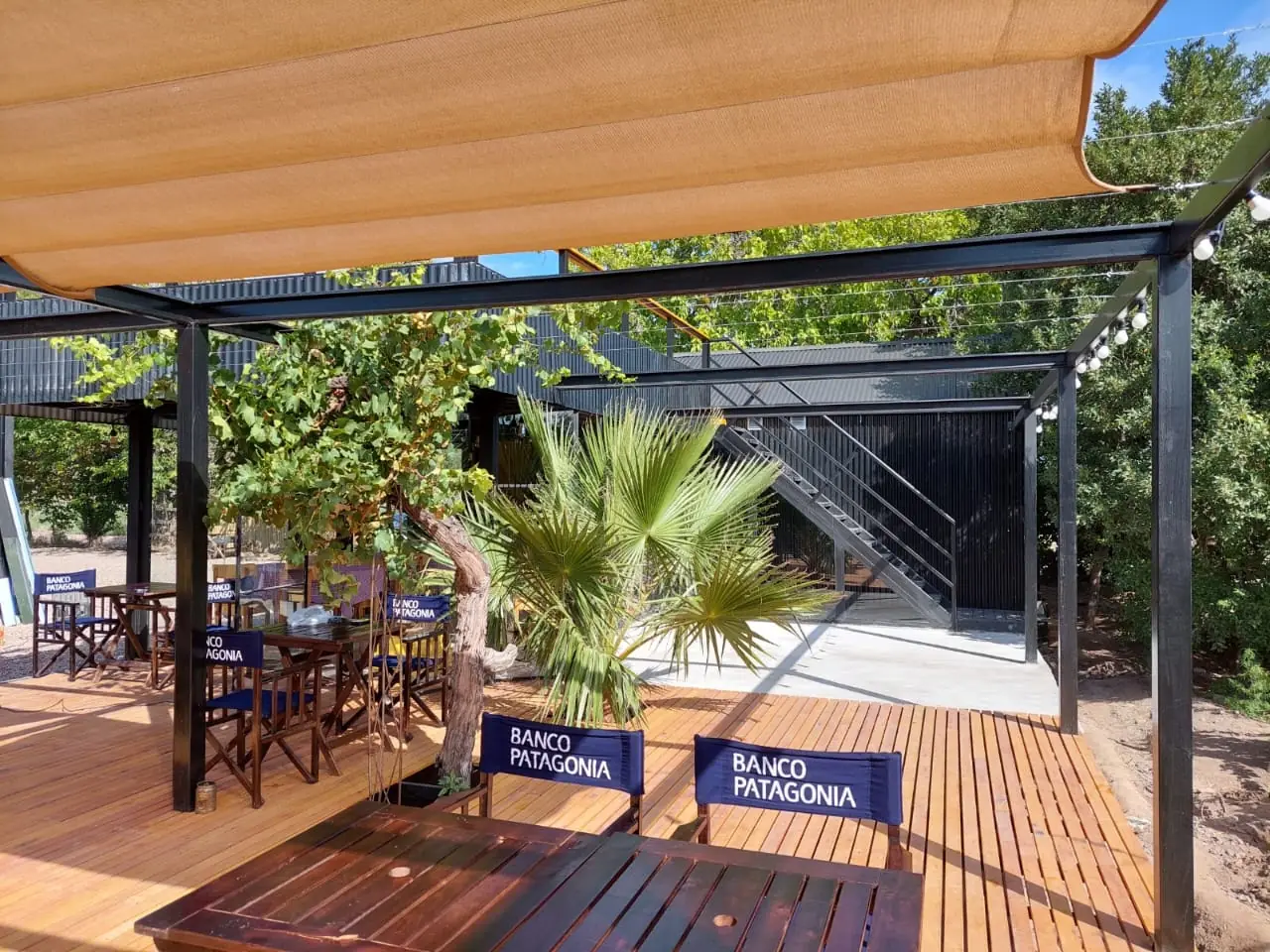 Mesas y sillas bajo la pérgola de lona clara sobre el deck de madera