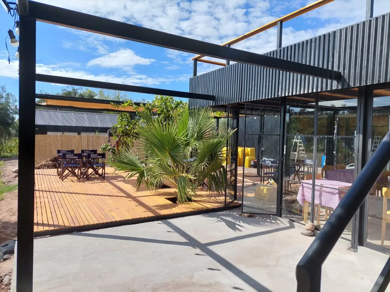 Deck de madera frente a la galería vidriada, con estructura metálica y palmera