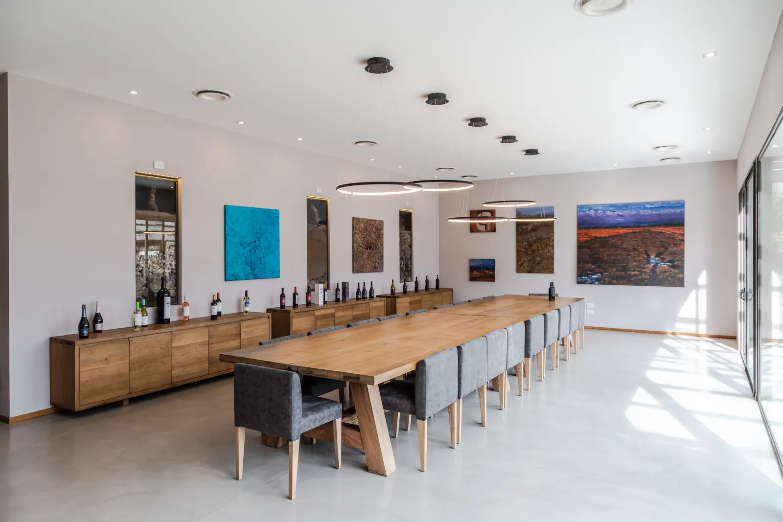Sala de degustación con mesa larga de madera, sillas tapizadas y obras de arte