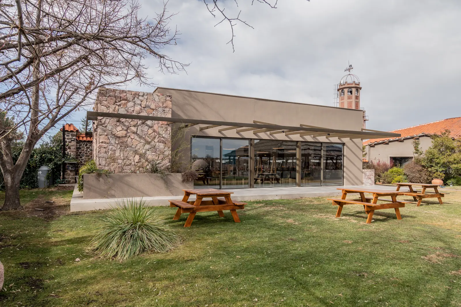 Frente del edificio sobre el césped, mesas de picnic y torre de la bodega