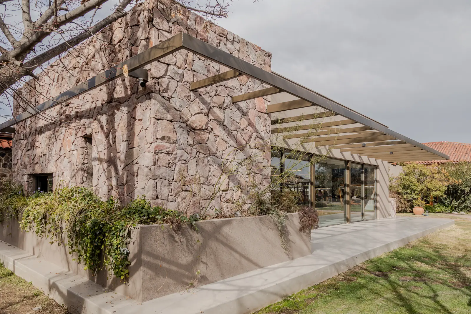 Muro de piedra con enredadera y pérgola en voladizo sobre la galería