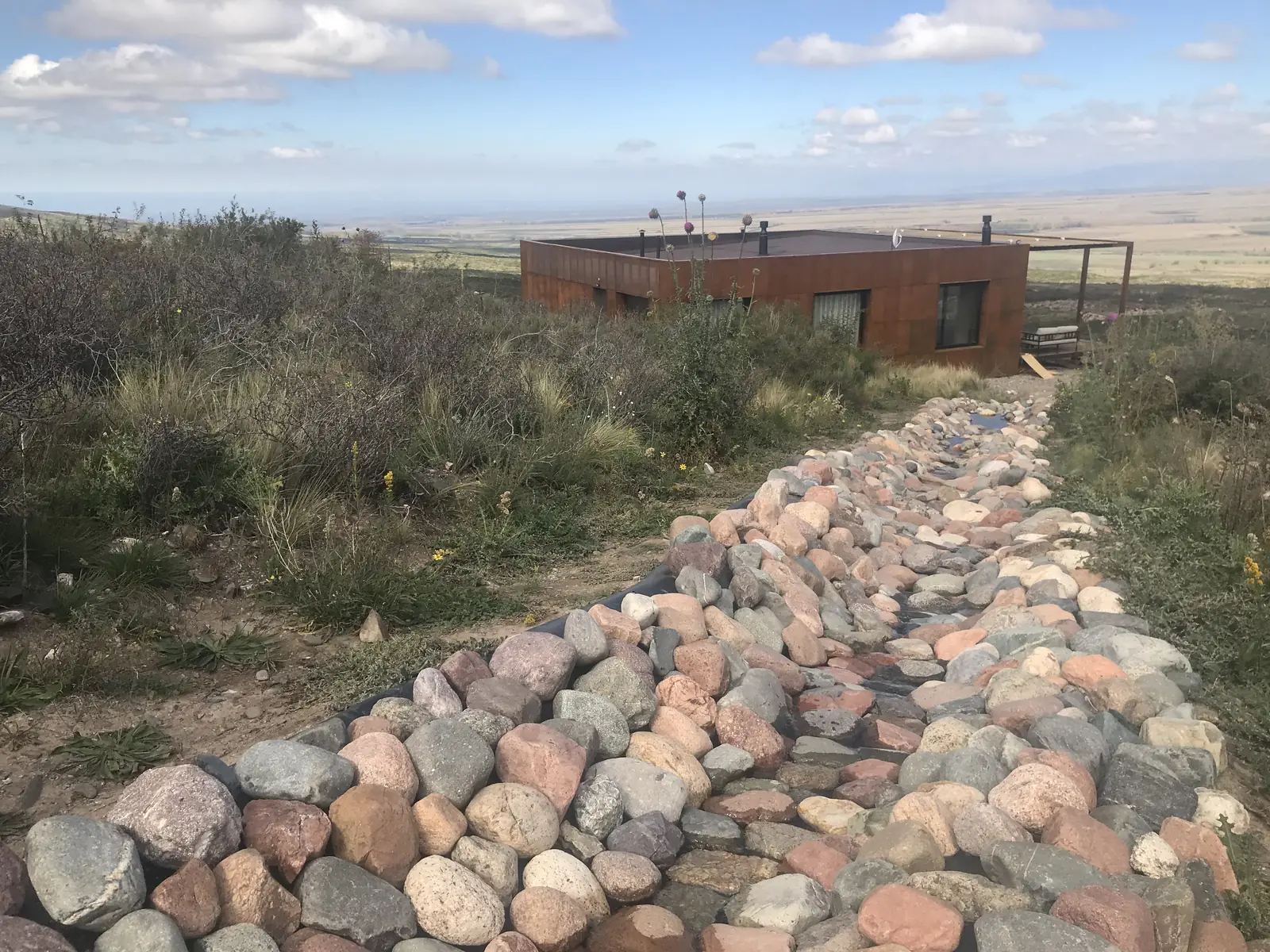 Sendero de piedras de río que sube hasta la casa de acero corten