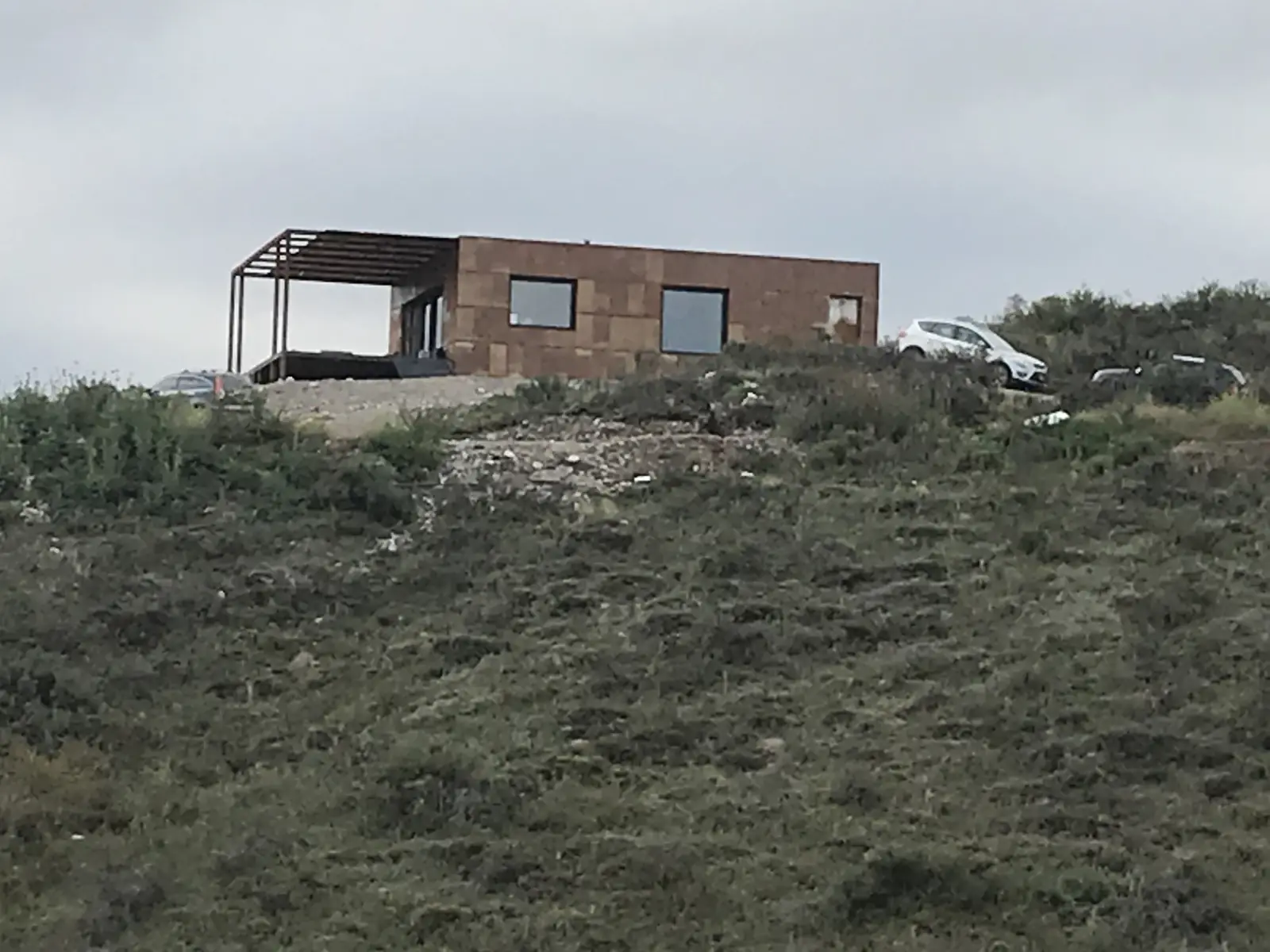 Vivienda en obra con pérgola metálica coronando la ladera de monte bajo