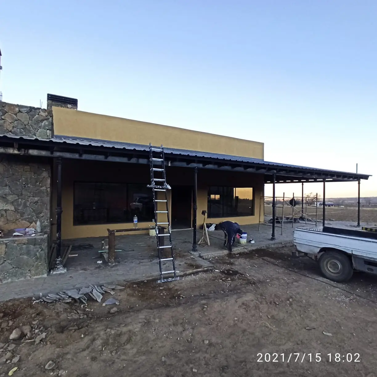 Frente en obra con galería de chapa, zócalo de piedra y andamio