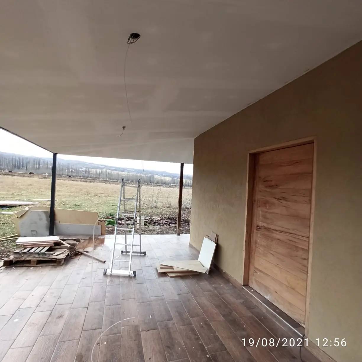 Galería con piso de madera, puerta maciza y vista al campo abierto