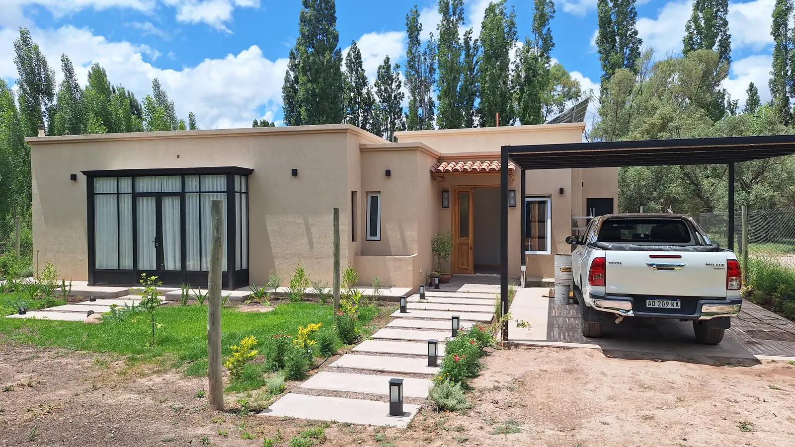 Frente de la casa con sendero de losetas, cantero y acceso cubierto