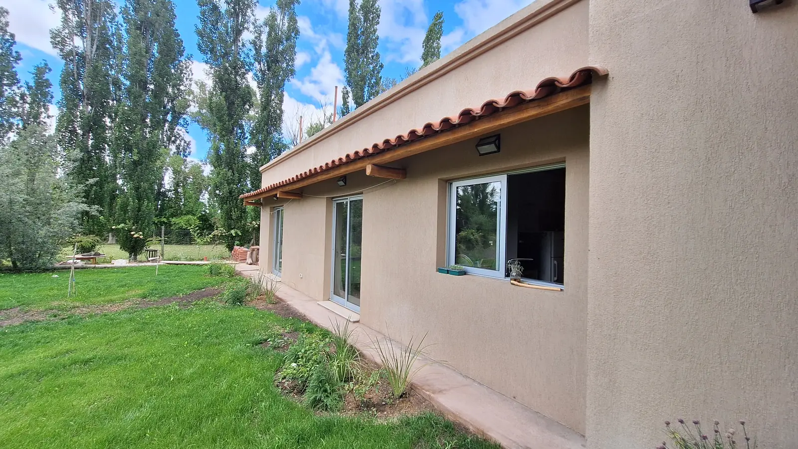 Lateral de la vivienda con ventanas, alero de tejas y césped nuevo
