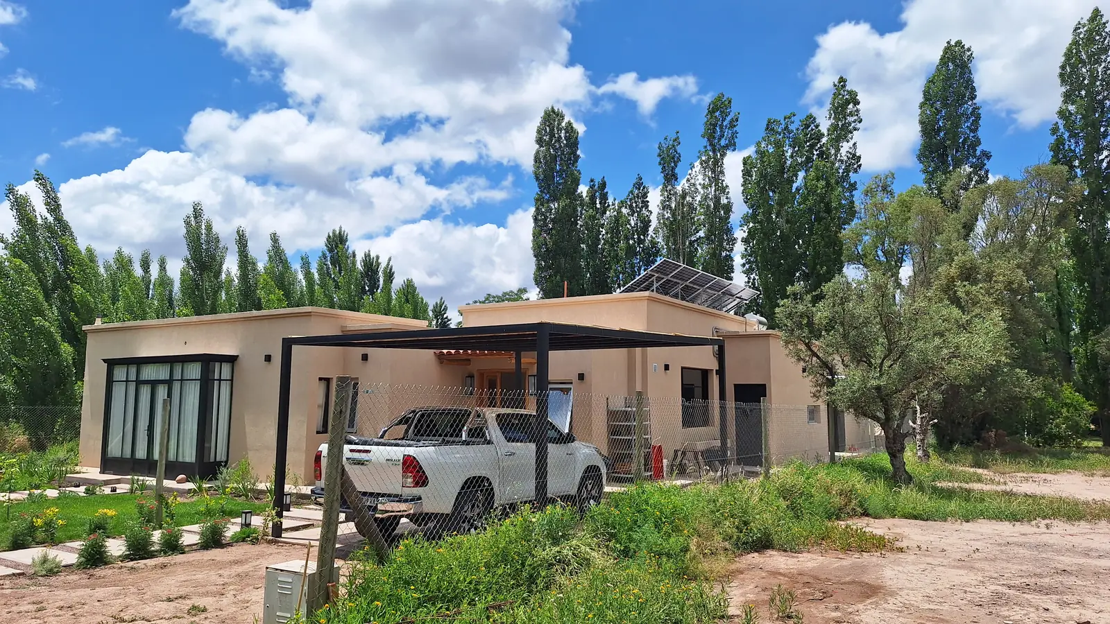 Vista general de la vivienda terminada con cochera metálica y jardín recién plantado