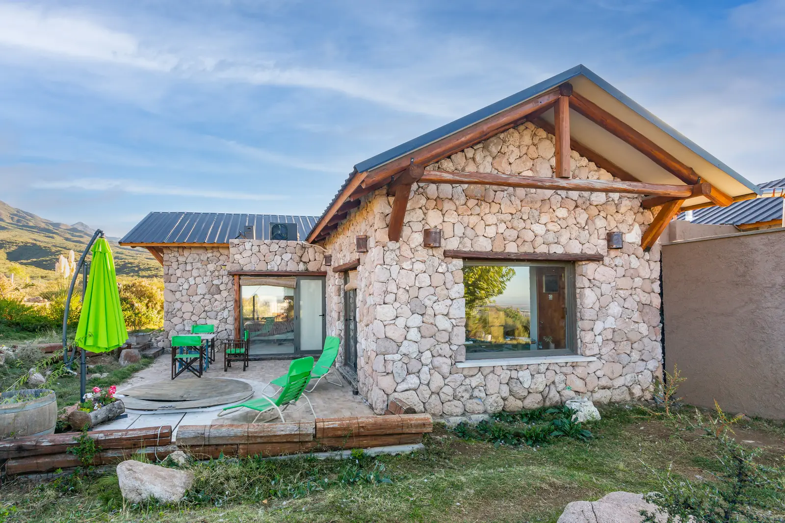 Frente de piedra con techo a dos aguas, galería y patio con sombrilla verde