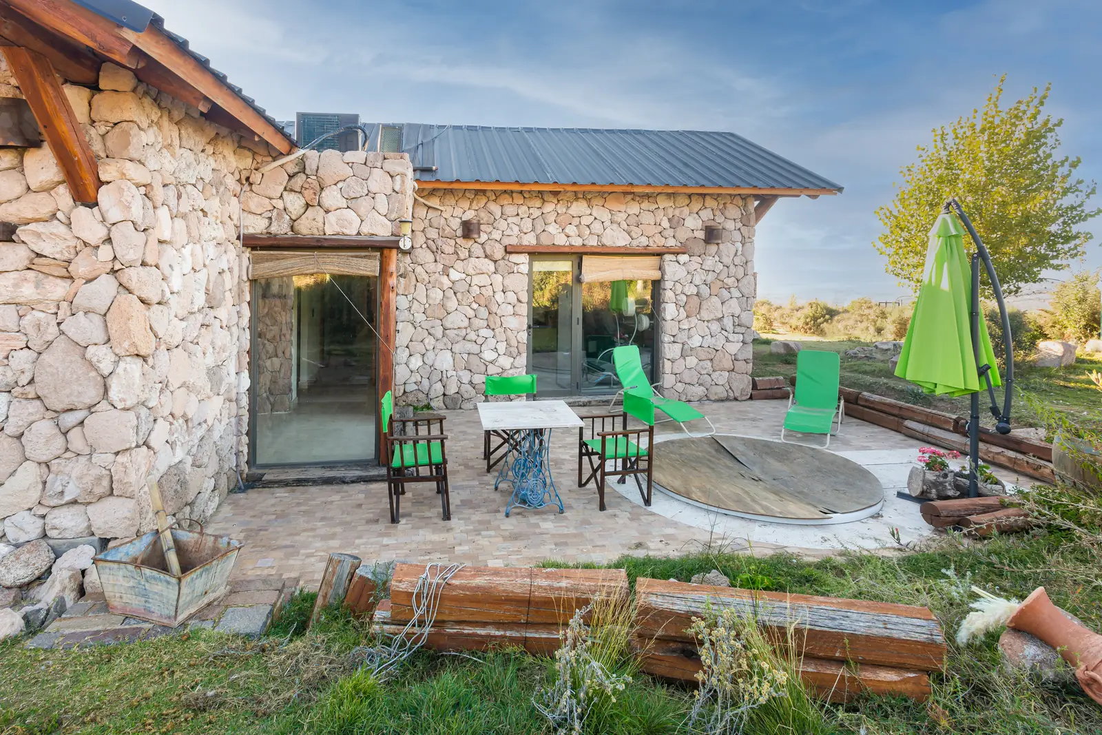 Patio de piedra laja con mesa, reposeras verdes y sombrilla junto a la casa