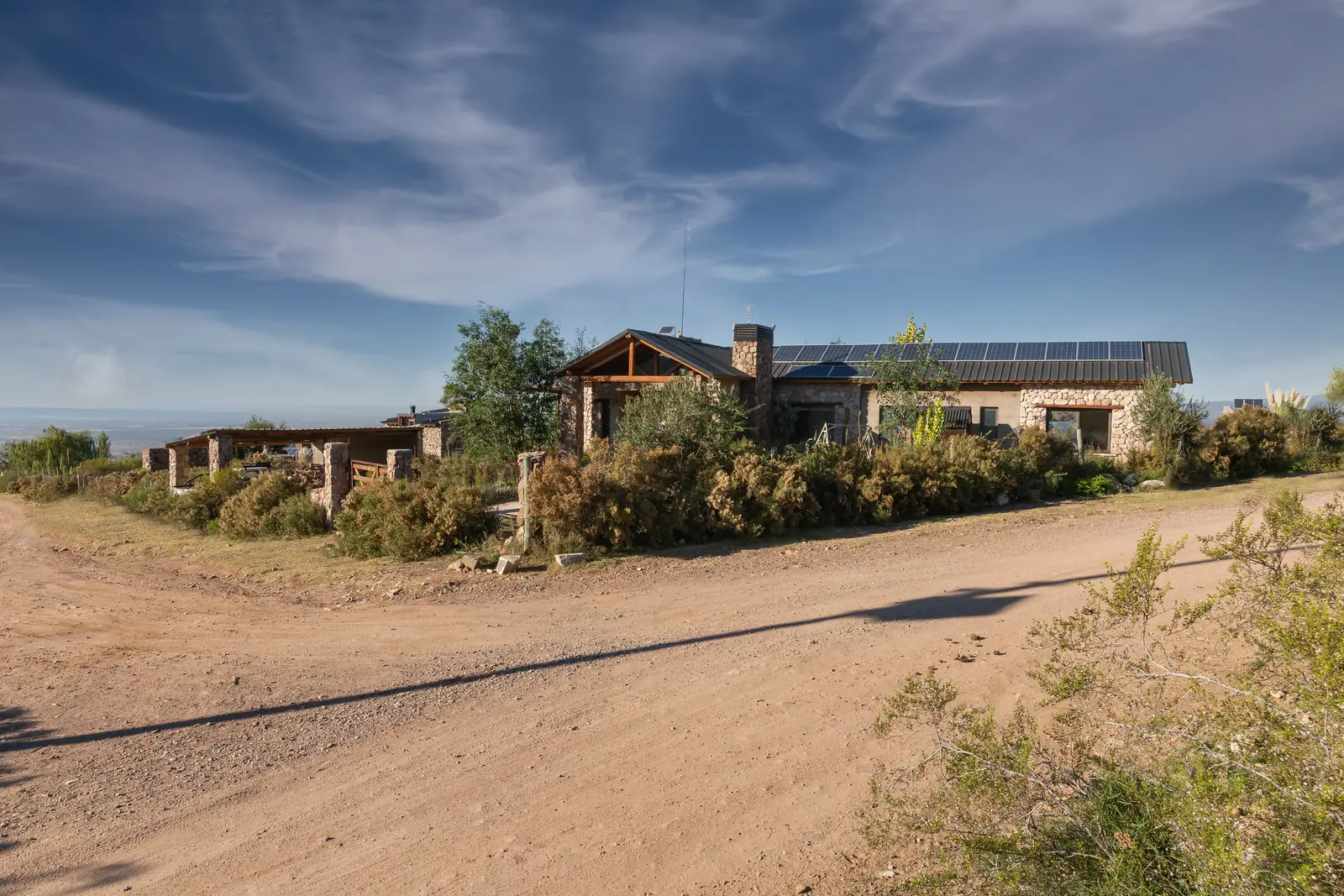 Casa vista desde el camino de tierra, recostada sobre el terreno con arbustos