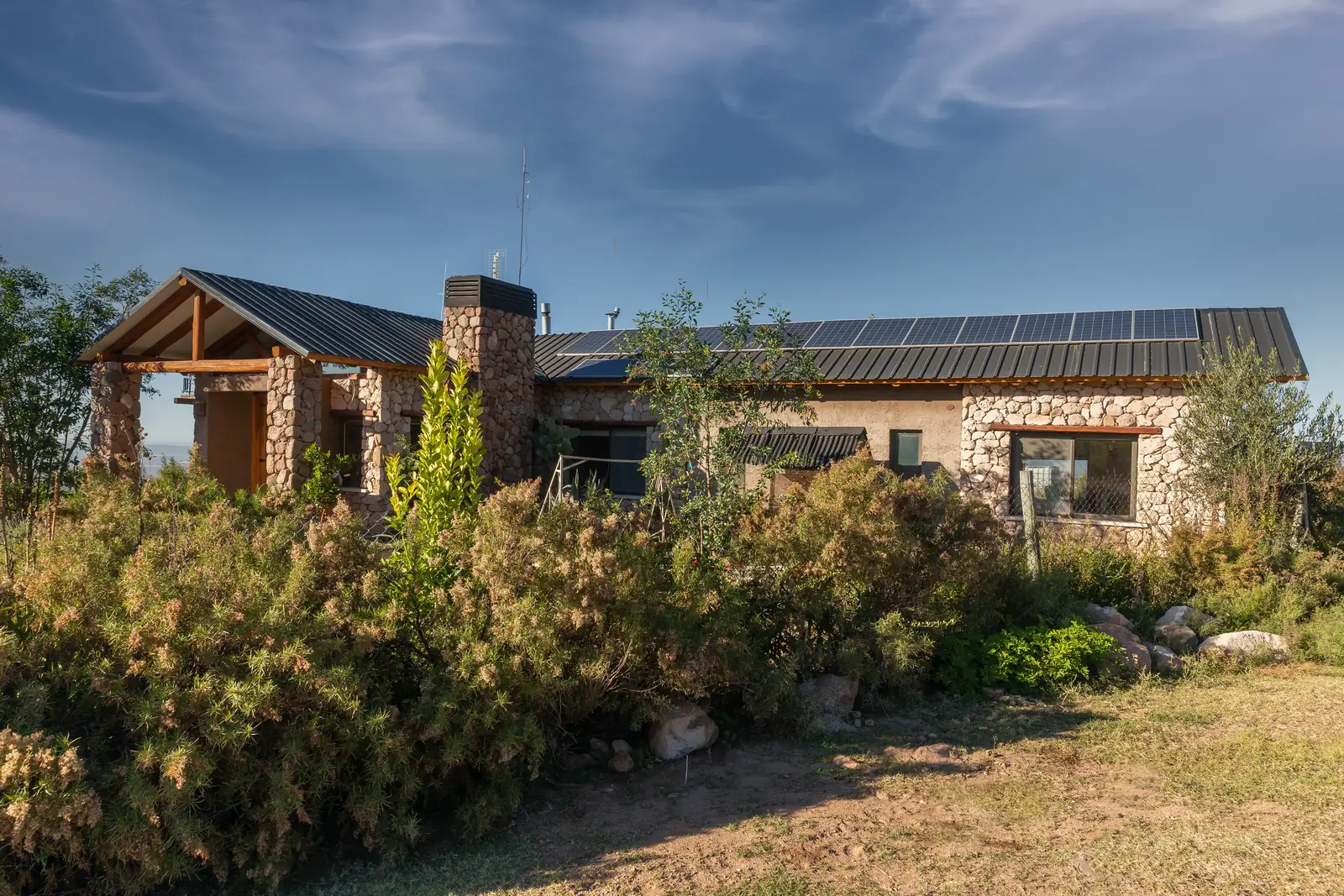 Volumen alargado con paneles solares en el techo, detrás de arbustos florecidos