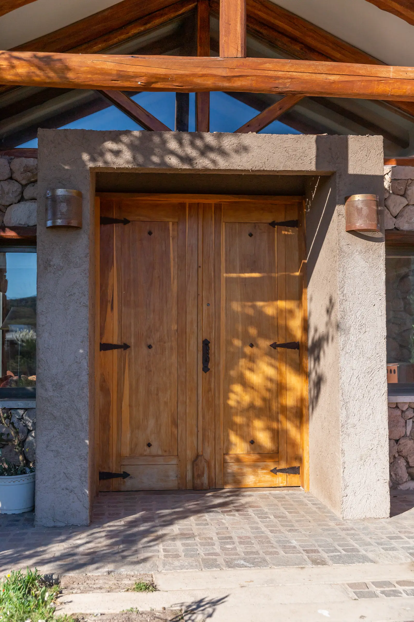 Puerta doble de madera enmarcada en hormigón, bajo cabriada de troncos