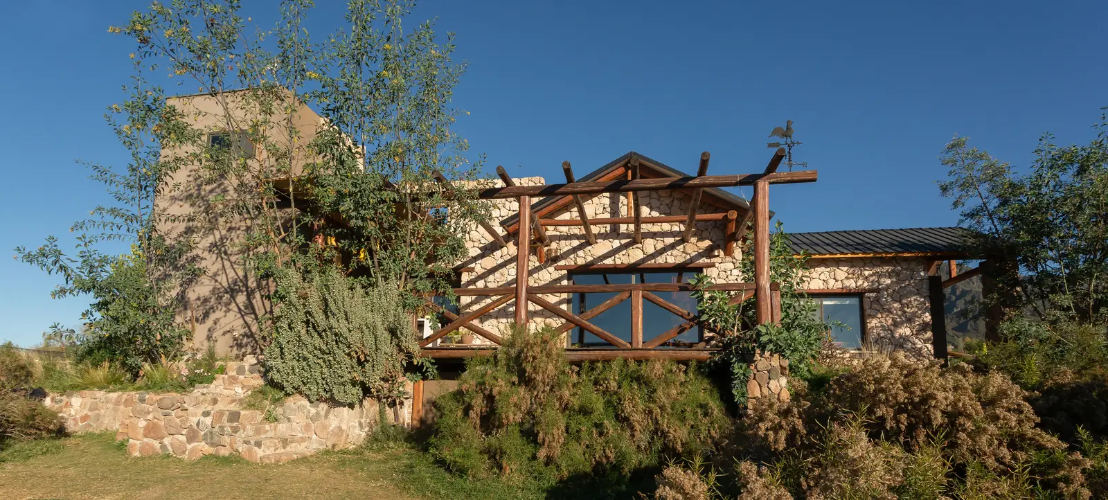 Vivienda de piedra sobre la loma con pérgola de troncos y torre lateral