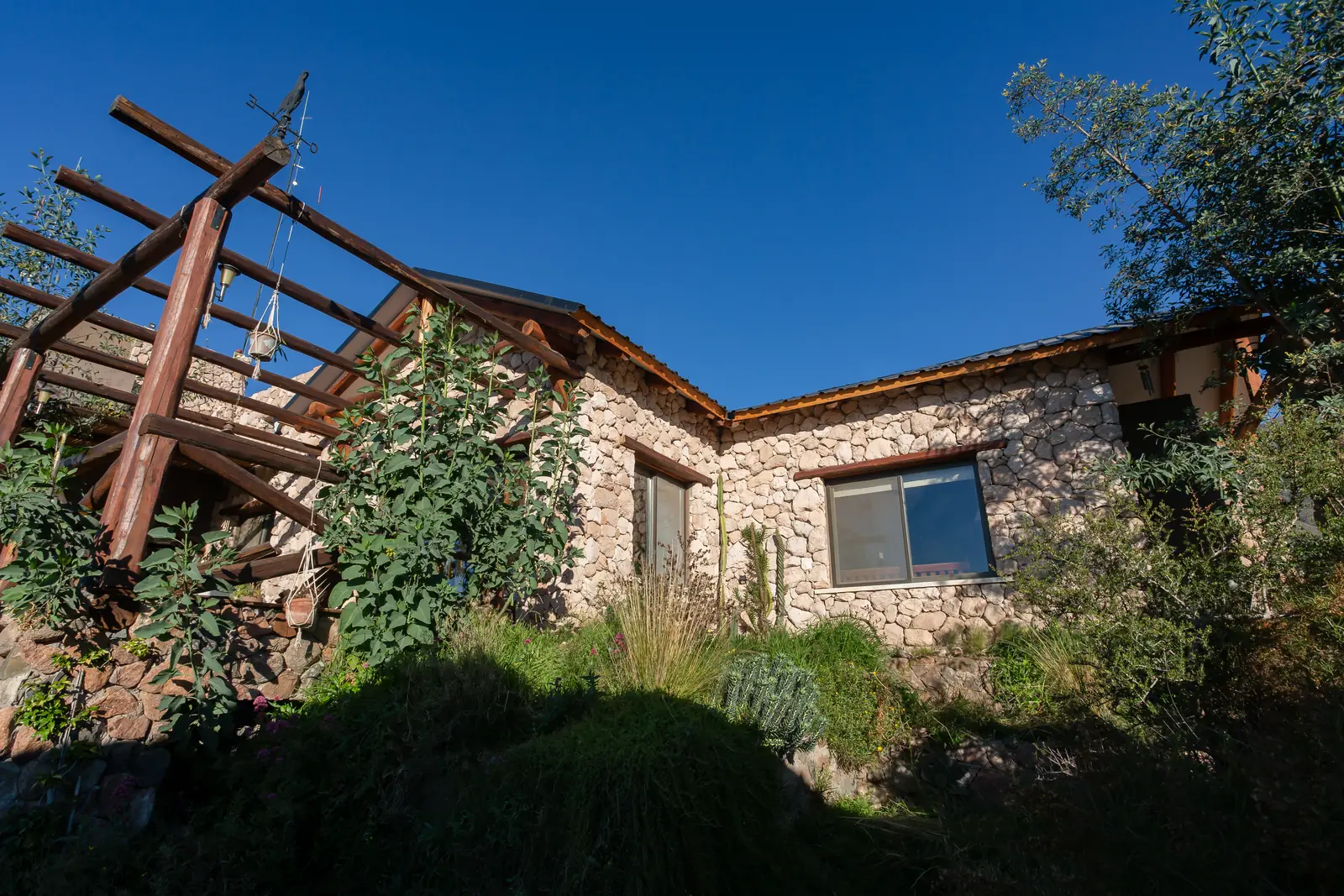 Casa de piedra con galería de troncos, rodeada de vegetación bajo cielo despejado