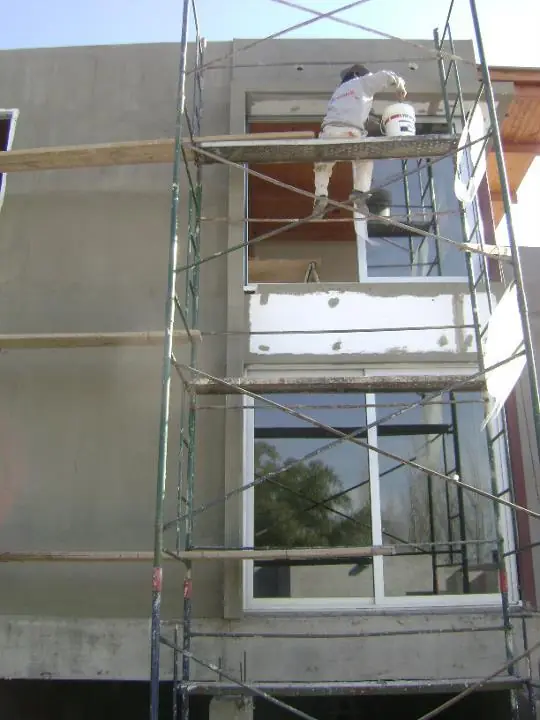 Operario revocando la fachada desde un andamio junto a las ventanas