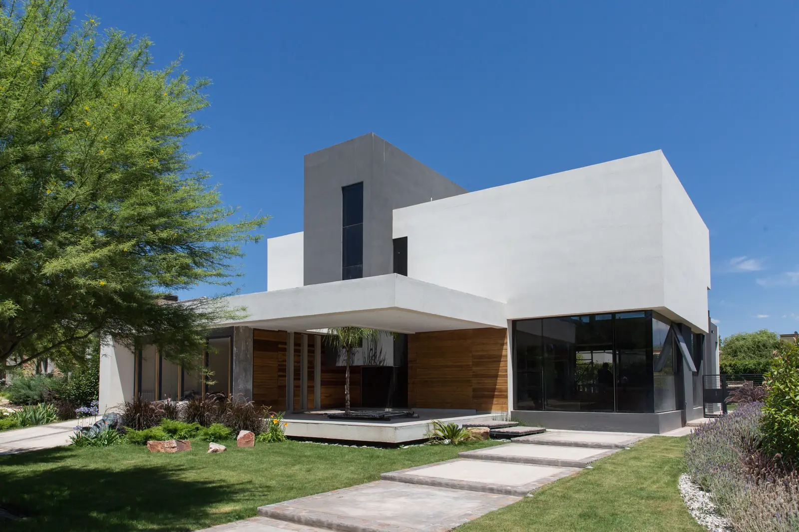 Frente de vivienda moderna de volúmenes blancos con jardín y sendero de acceso