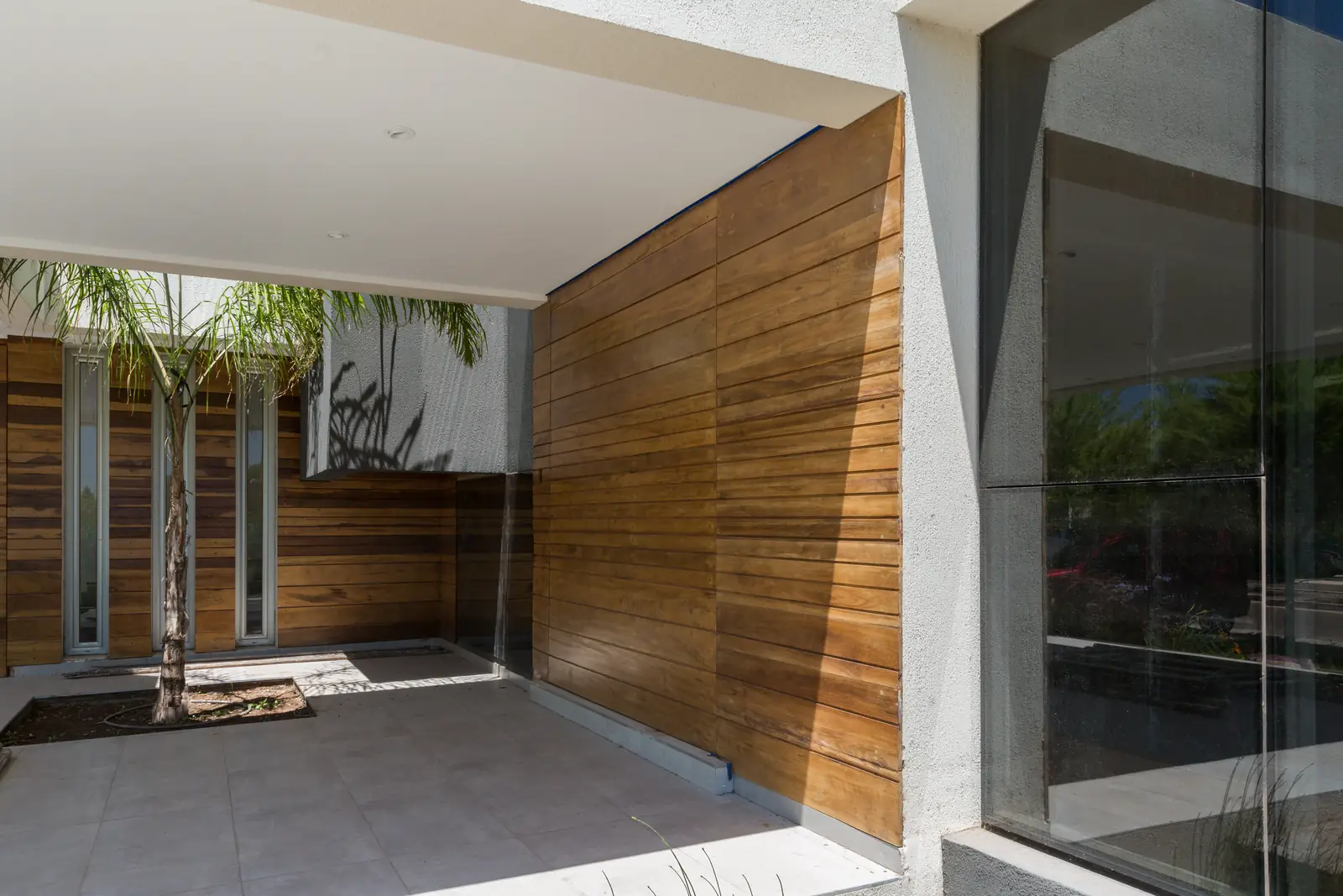 Acceso cubierto revestido en madera con grandes paños vidriados hacia el jardín