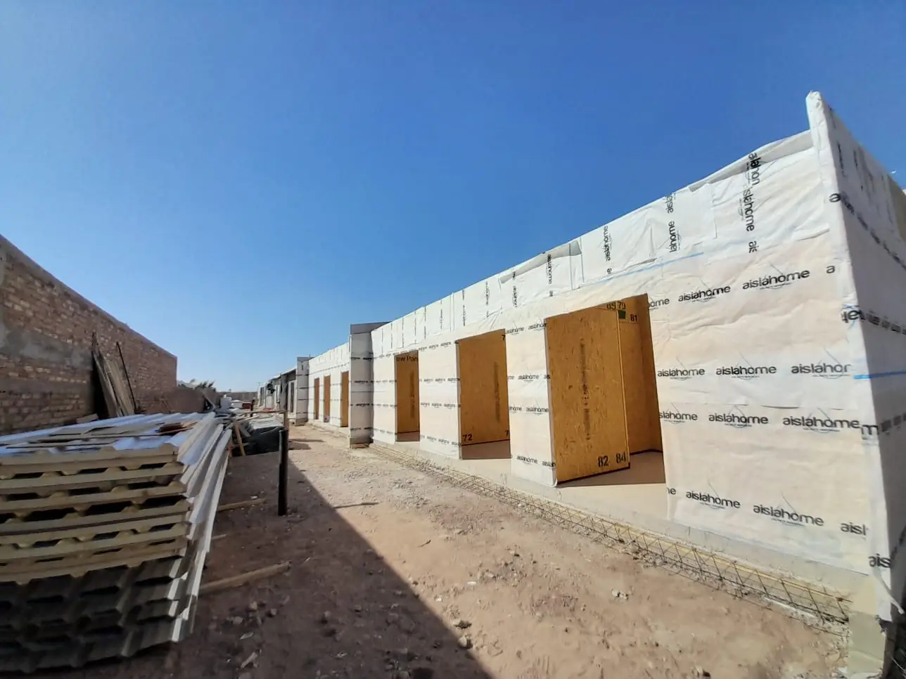 Perspectiva de la fila de viviendas de paneles SIP con pallets de material