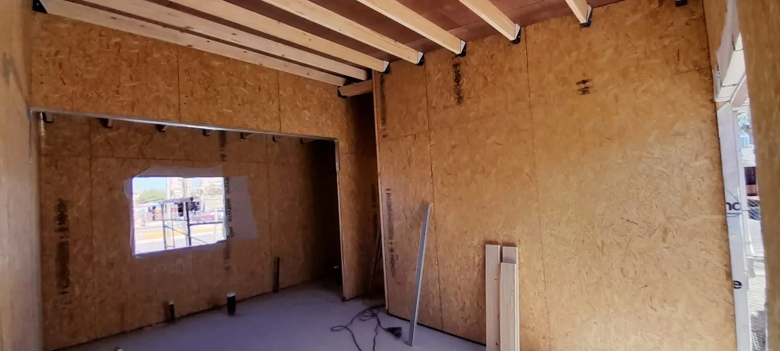 Ambiente interior con muros de OSB, ventana y estructura de techo de madera