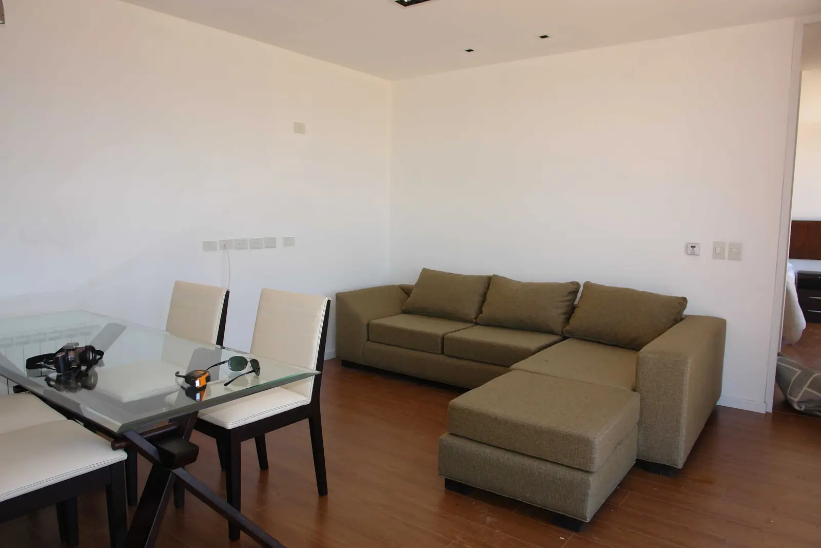 Estar comedor con sofá esquinero, mesa de vidrio y piso de madera