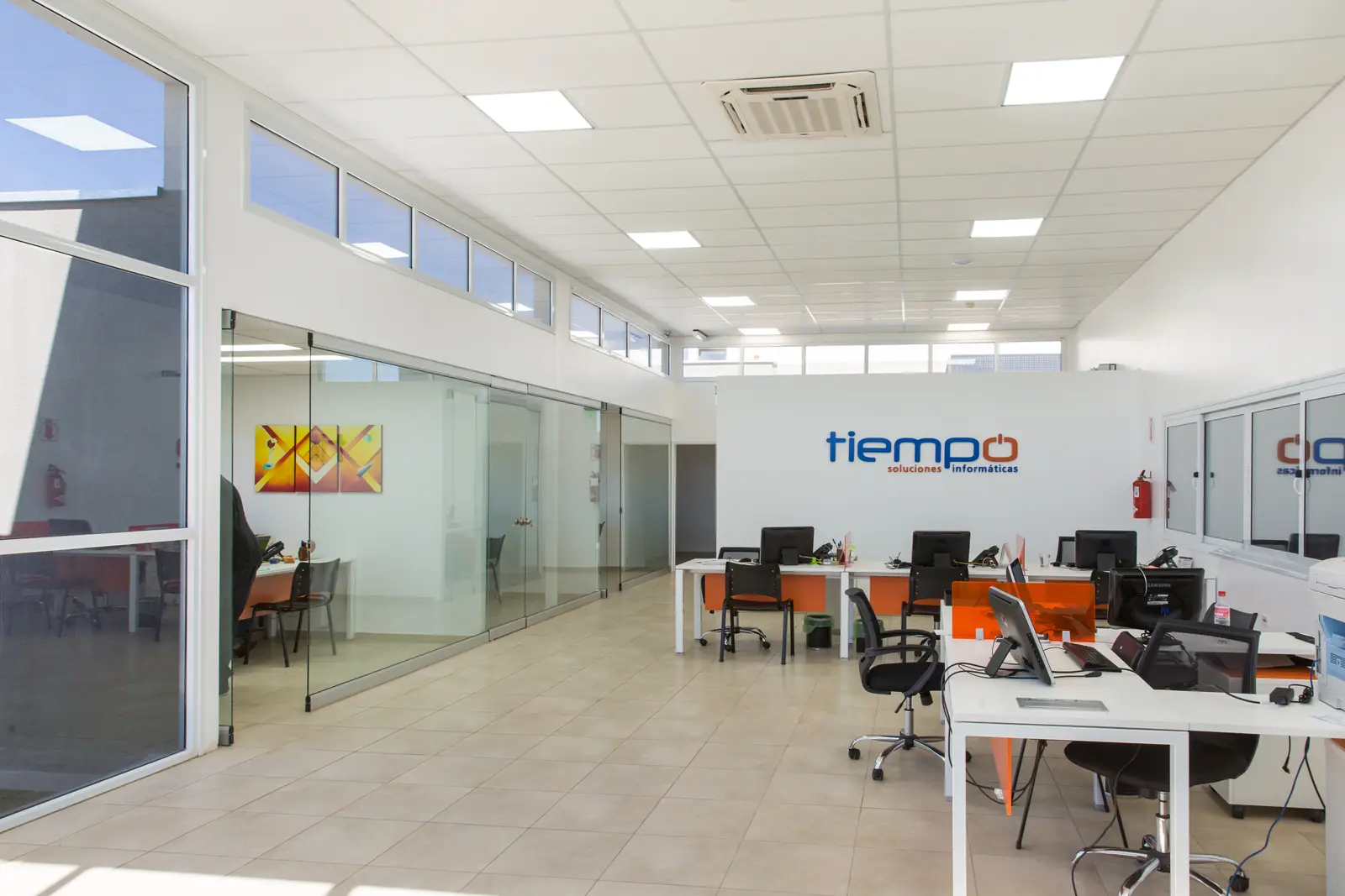Oficina abierta con escritorios, sillas y tabiques vidriados iluminada por luz natural