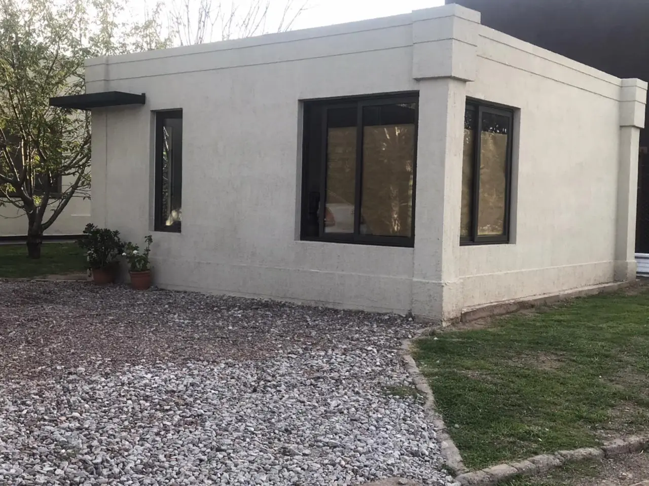 Frente de la vivienda terminada con ventanas negras y césped delantero