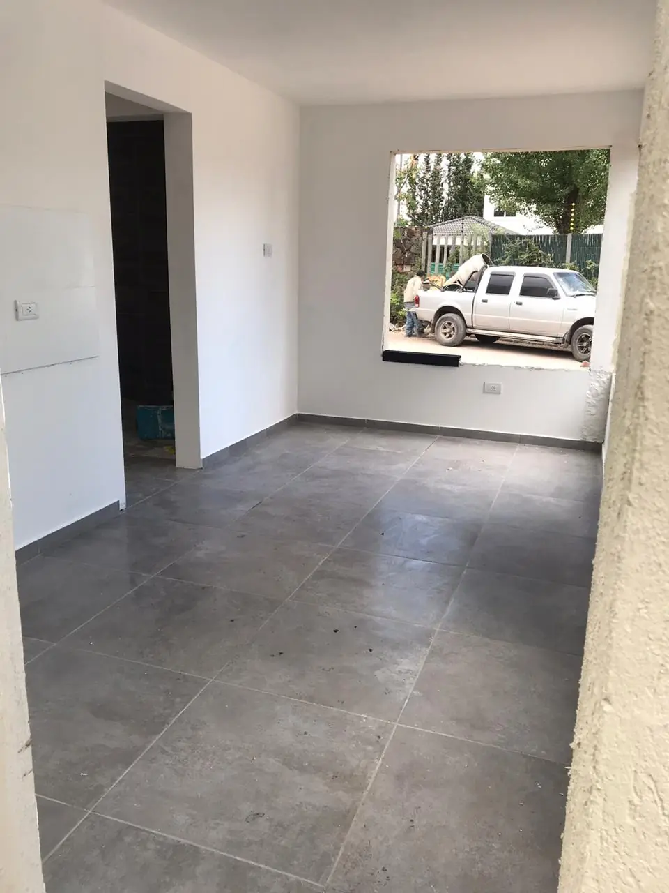 Ambiente interior terminado con porcelanato gris y vano hacia el exterior