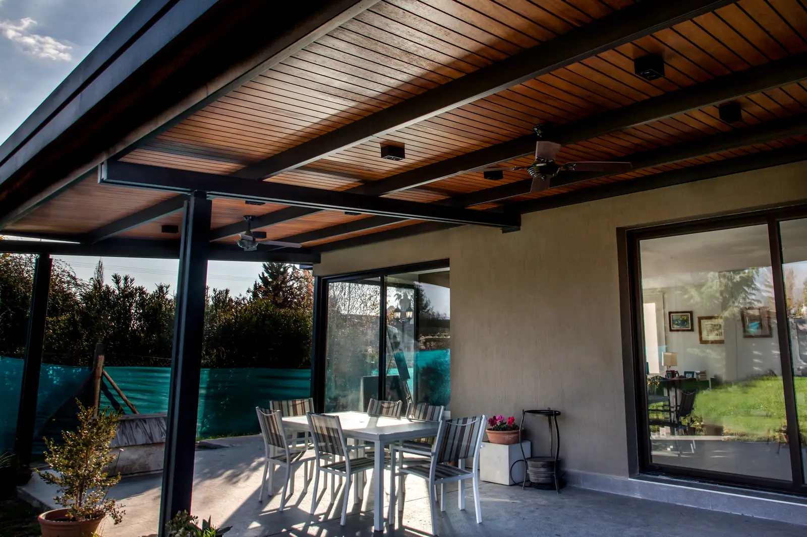 Galería con cielorraso de madera, pérgola metálica y mesa exterior