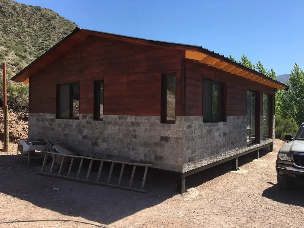 Vivienda terminada con revestimiento de madera y zócalo de piedra entre cerros