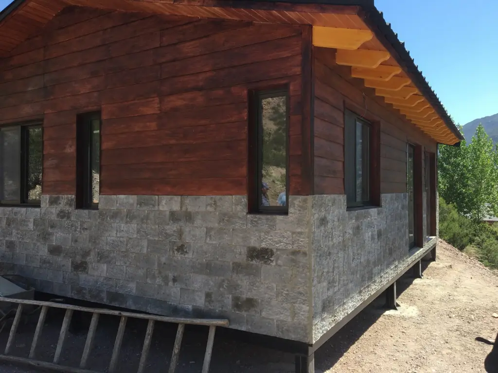 Vista lateral de la vivienda con carpinterías oscuras y alero de madera