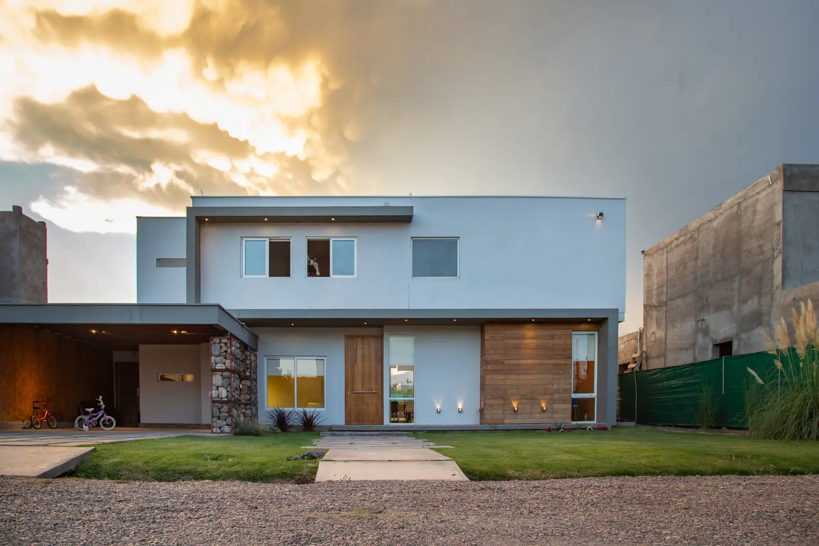 Frente de la casa de dos plantas al atardecer, césped y sendero de acceso