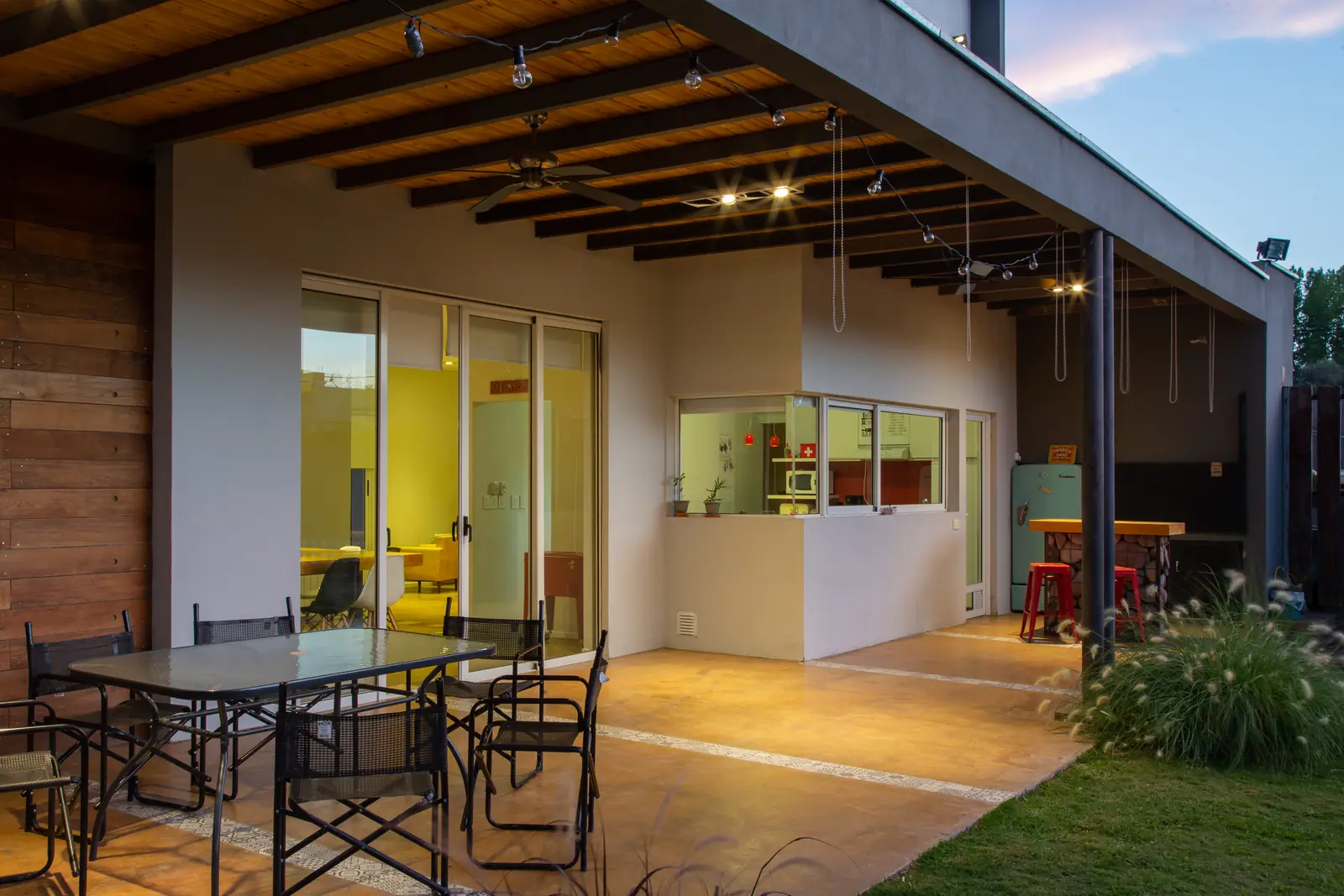 Galería con techo de vigas de madera, mesa de hierro y cocina al fondo