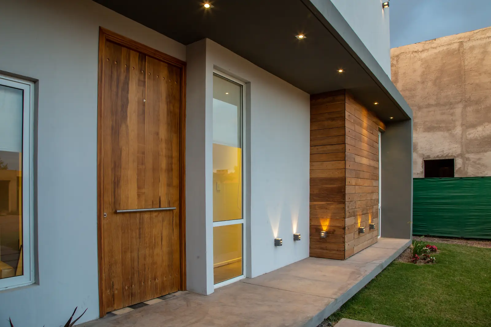 Puerta de ingreso de madera maciza y revestimiento de madera con luces empotradas