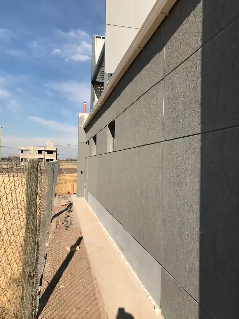 Fachada lateral con revestimiento gris de placas y vereda perimetral