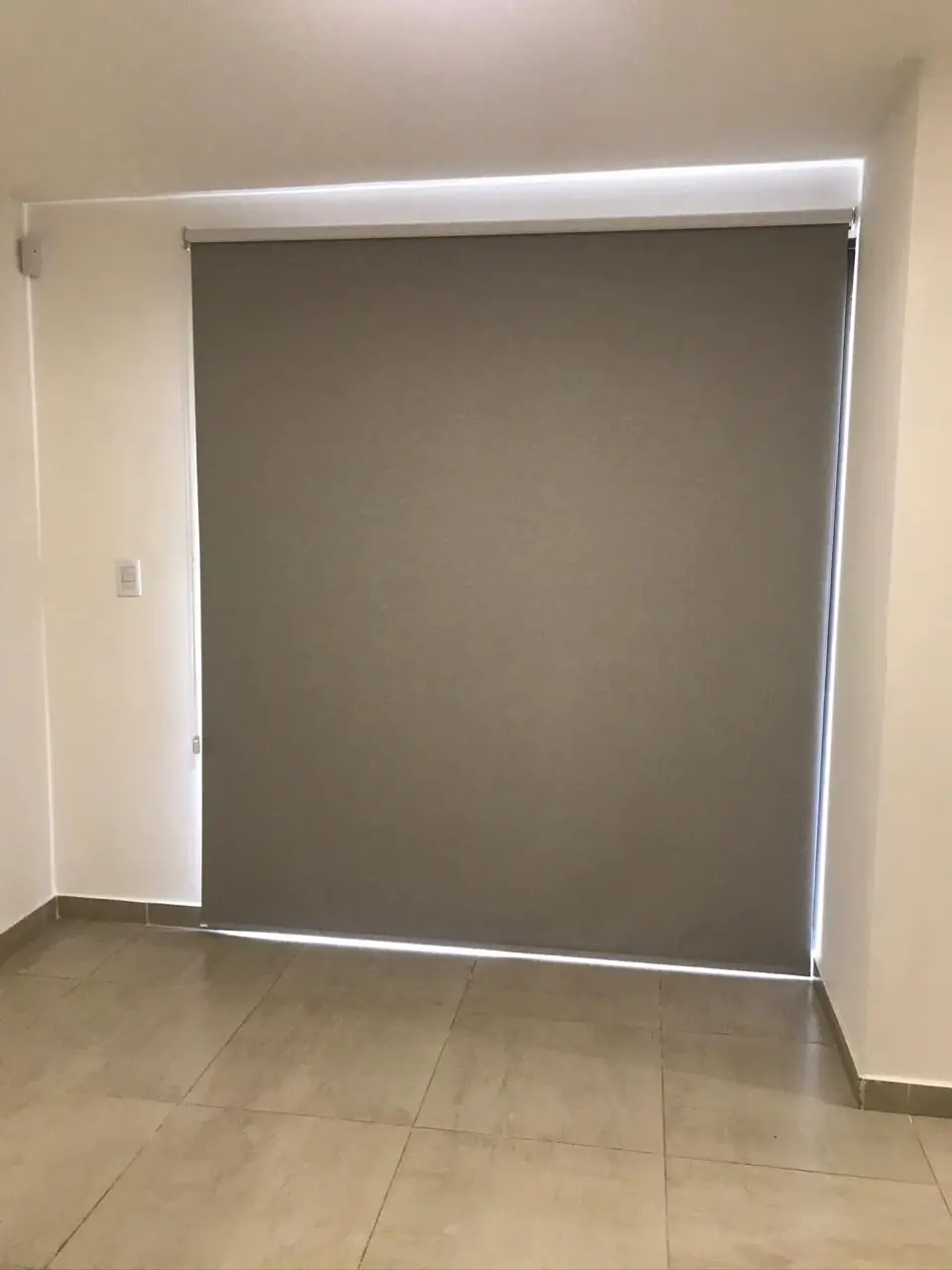 Ambiente interior vacío con pared gris, piso de porcelanato y cortina roller