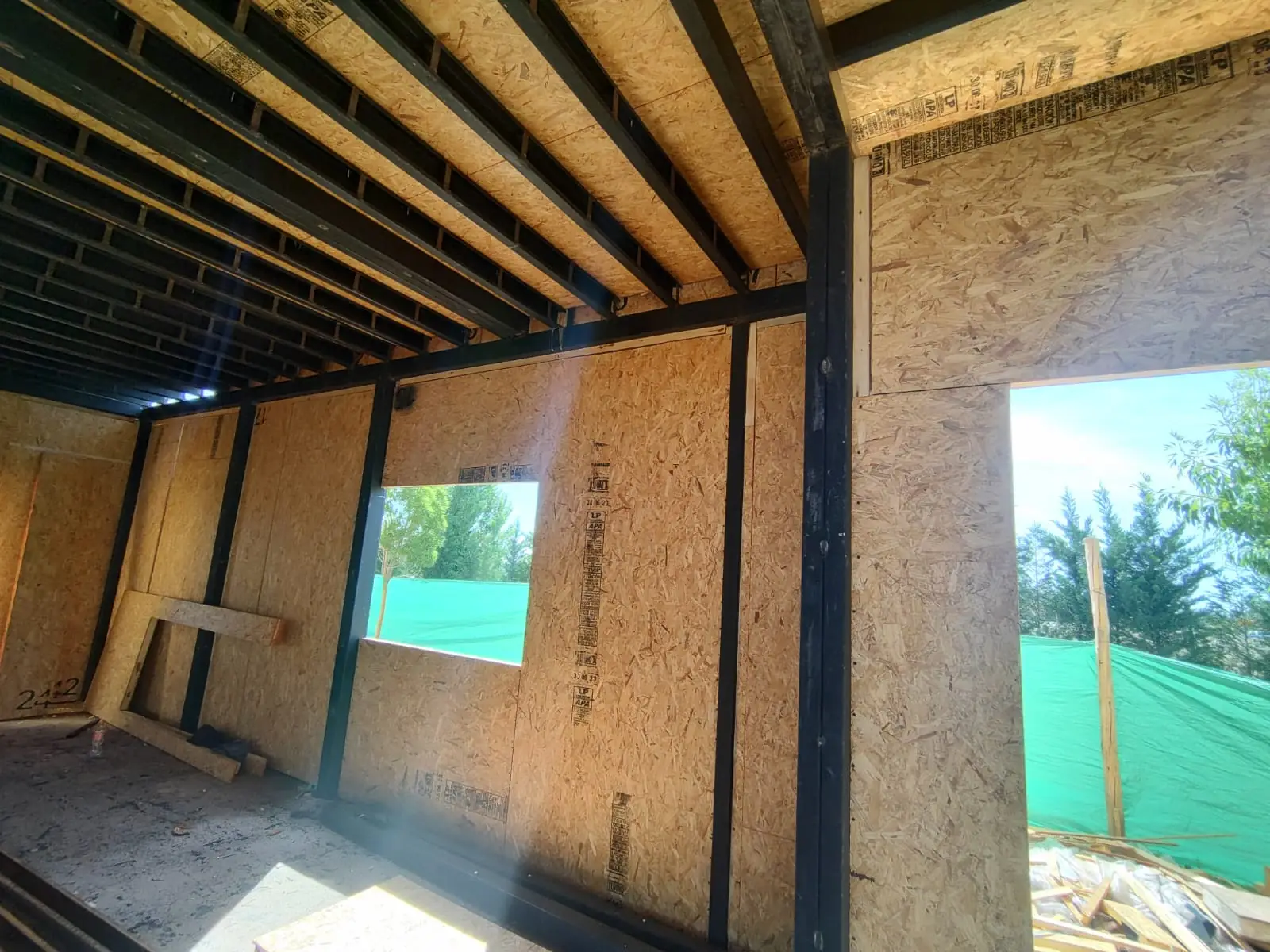 Interior en obra con muros de panel SIP y vanos hacia el jardín