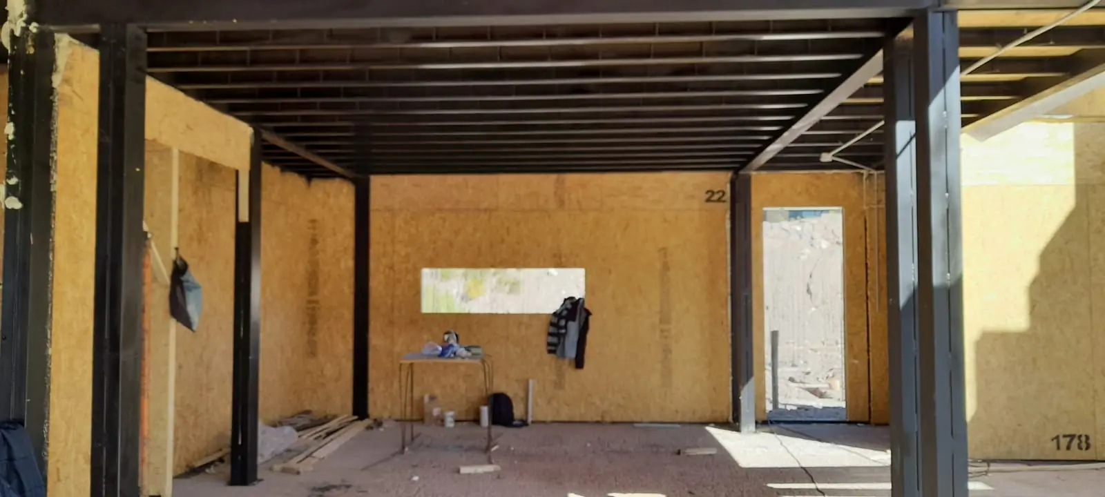 Ambiente longitudinal en obra con estructura de techo y puerta al fondo