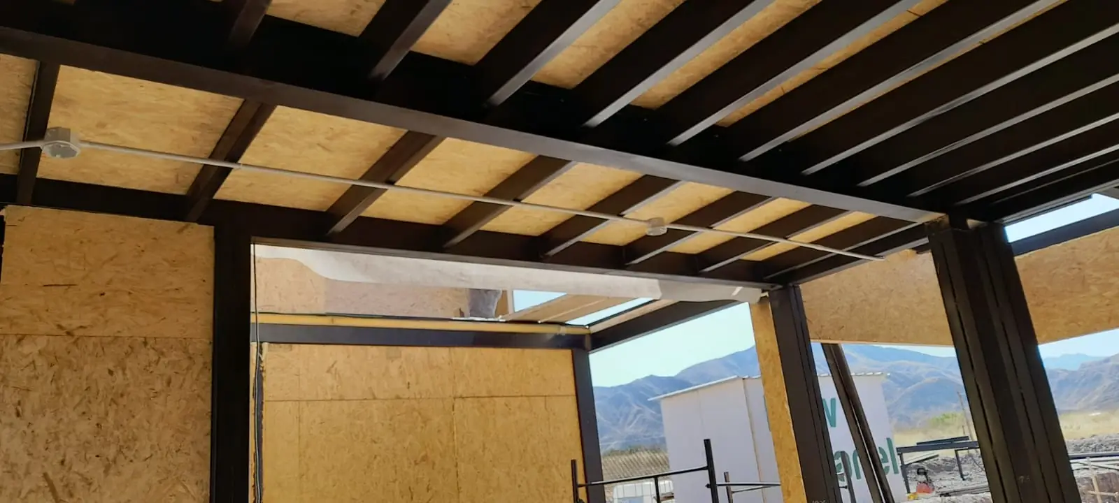 Interior con perfiles metálicos de techo y abertura hacia el paisaje serrano