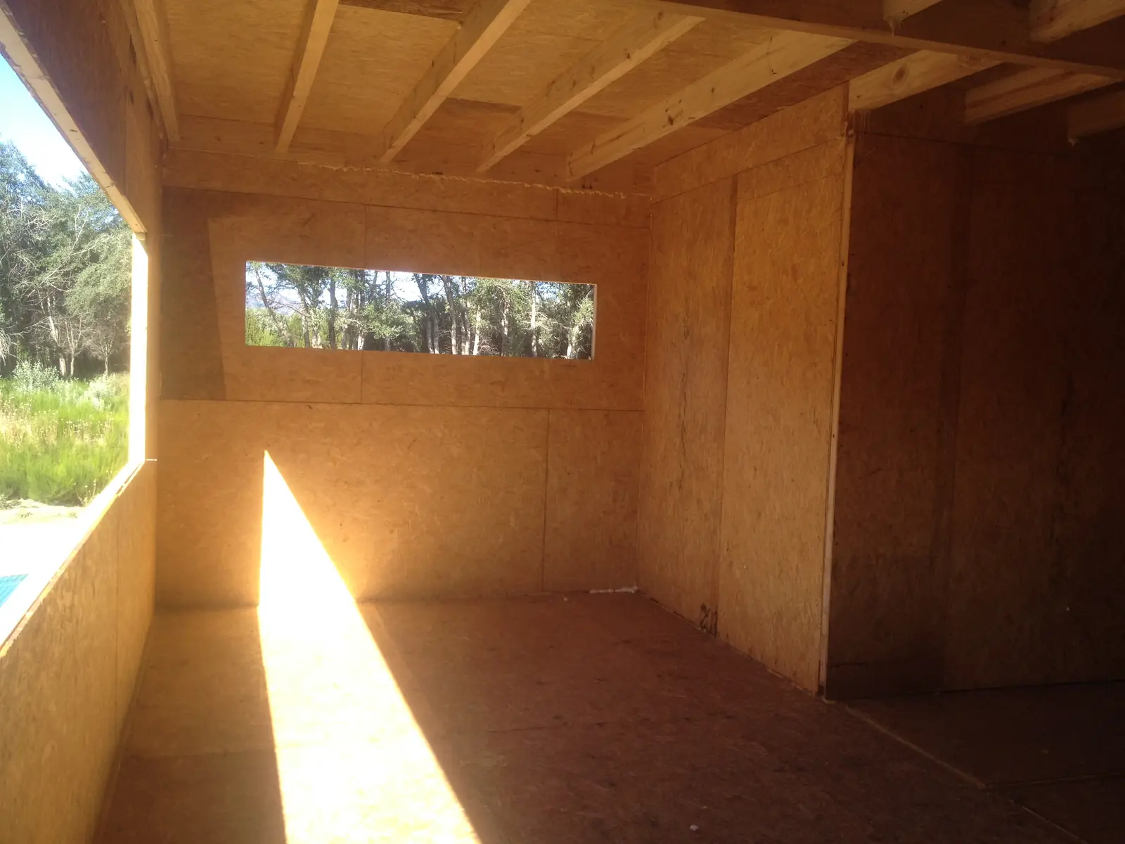 Interior en bruto con vano alto al fondo y sol sobre el piso de OSB